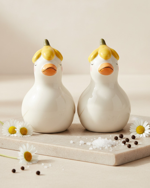 Two white duck-shaped salt and pepper shakers on a wooden board with flowers and spices.