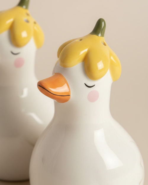 Two ceramic duck-shaped figures with yellow heads and orange beaks on a beige background.