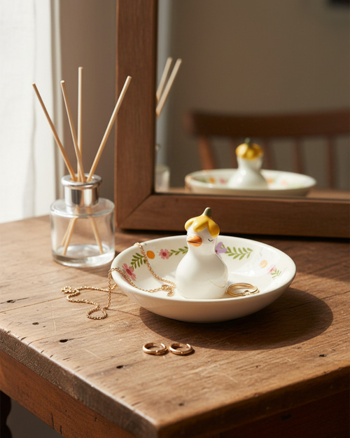 Decorative duck-shaped jewelry dish on a wooden surface with a diffuser and mirror in the background.