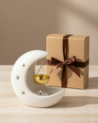 Decorative moon-shaped candle holder with a lit candle next to a wrapped gift box on a wooden surface.