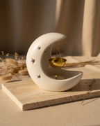 Ceramic moon-shaped incense burner with a gold bowl on a wooden surface.
