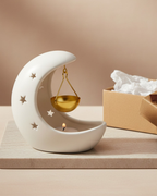 Decorative ceramic moon-shaped holder with a candle and gold weight on a wooden surface.